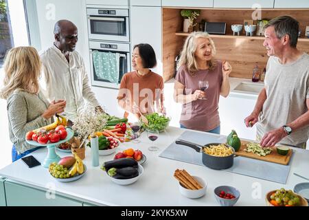 Eine Gruppe von Seniorfreunden, die Wein tranken, während sie sich in der Küche versammelten Stockfoto