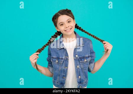 Ein glückliches Mädchen mit Schönheitslook hält lange Haarsträhne in legerer Mode, blauer Hintergrund, Frisur Stockfoto