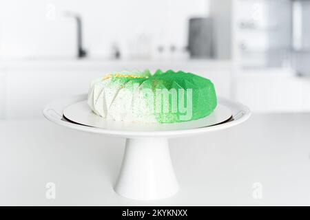 In der weißen Küche auf dem Tisch ist ein grüner Moussekuchen auf einem weißen Ständer mit einem Bein Stockfoto