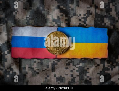 Russische und ukrainische Flaggen, Bitcoin in der Mitte, Tarnhintergrund Stockfoto