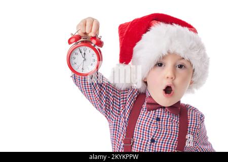 Weihnachtsjunge mit rotem Wecker, lächelndem kleinen Mann in rotem weihnachtsmannhut, Krawatte und Strumpfhalter auf weißem Hintergrund Stockfoto