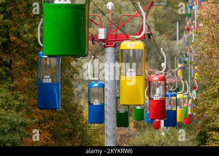 Farbenfrohe rot-grün-blau-gelbe Seilbahn-Hütten im Vergnügungspark Kharkiv mit Herbstbäumen Stockfoto