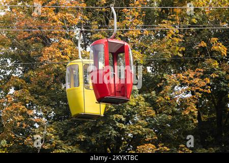 Farbige rote und gelbe Seilbahnkabinen im goldenen Herbstpark. Standseiltransport auf Metalldrähten Stockfoto