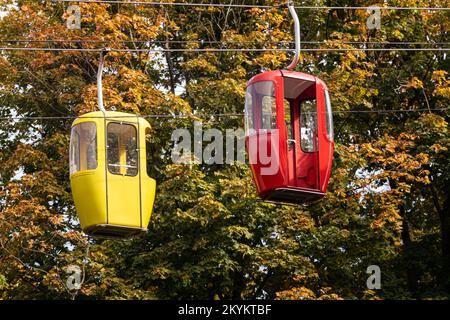 Farbige rote und gelbe Seilbahnkabinen in Herbstbäumen. Standseiltransport auf Metalldrähten Stockfoto