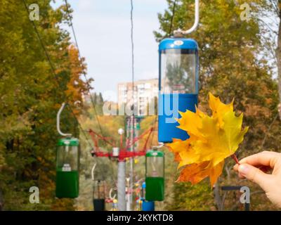 Halten Sie farbenfrohe Herbstblätter in der Seilbahn im Vergnügungspark von Charkiv. Kabelkabinen in Herbststimmung Stockfoto
