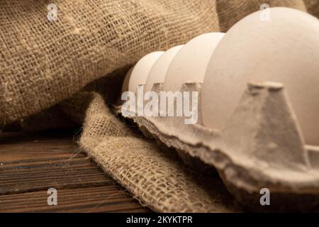 Weiße Hühnereier in einer Pappschachtel auf dem Tisch. Nahaufnahme, selektiver Fokus Stockfoto