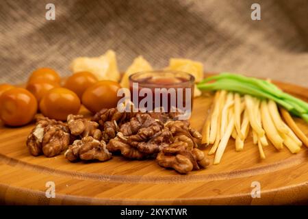 Verschiedene Sorten von Käse, Walnusskernen, geräucherten Wachteleiern und Honig in einer Glasvase auf einer Holzoberfläche. Stockfoto