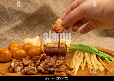 Jemand taucht ein Stück Käse in Honig vor dem Hintergrund verschiedener Käsesorten Stockfoto