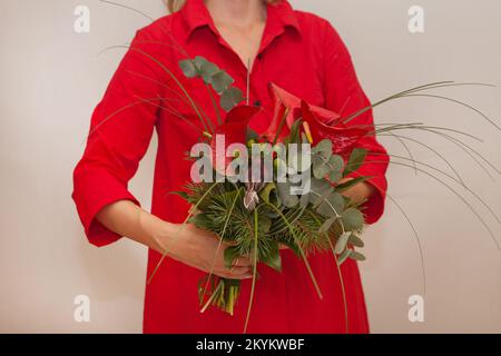 Roter weihnachtsstrauß. Frauenhände mit Calla-Blume. Dekoration mit Vogel, Brunia und Tanne. Feiertage Stockfoto