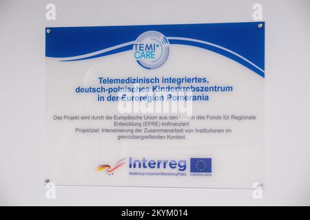 01. Dezember 2022, Mecklenburg-Vorpommern, Greifswald: Ein Schild mit den Worten "Telemedizin integriertes deutsch-polnisches Kinderkrebszentrum in der Euroregion Pommern" hängt hinter einem NM/CT 870 DR-Gerät von General Electric Medical Systems, Israel, in den Räumen der Kinderklinik des Universitätsklinikums Greifswald. Dieses SPECT/CT-System ermöglicht noch präzisere nuklearmedizinische Untersuchungen. Dies ist für spezielle Behandlungsoptionen wie die Radioisotopentherapie erforderlich. Die Computertomographie (CT) verwendet eine große Anzahl von Röntgenbildern zur Berechnung digitaler Bilder. Ein SPECT-Scan, auf t Stockfoto