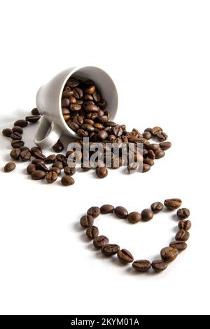 Verschüttete Kaffeebohnen aus einer Tasse mit einem Herzmuster. Stockfoto