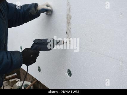 Bauunternehmer, der die thermische Außenwanddämmung installiert. Isolierende Hauswände mit Hartschaumplatte. Stockfoto