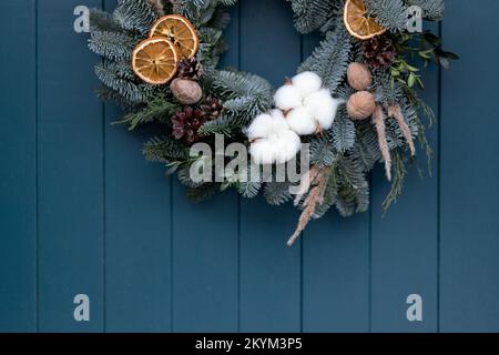 Weihnachtskranz auf dem Hintergrund einer blauen Holztür. Neujahrsdekor mit eigenen Händen Stockfoto