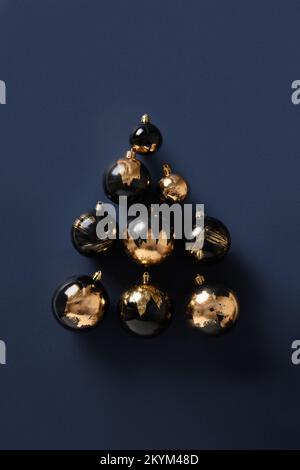 Alternativer moderner Weihnachtsbaum aus goldenen und schwarzen Kugeln auf blauem Hintergrund. Dekorative Kugeln in Form eines Weihnachtsbaums. Weihnachtsgrüße Stockfoto