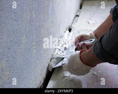 Füllung einer strukturierten Wand mit einer breiten Kelle Nahaufnahme, Auftragen von elastischem Kitt auf die vorbereitete Oberfläche einer Raumwand Seitenansicht, die Arbeit eines Putzers Stockfoto