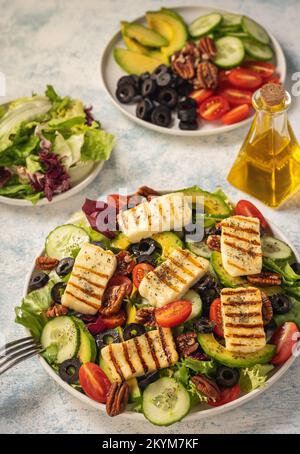 Griechische Küche - Salat mit gegrilltem Halloumi-Käse, Avocado, Pekannüssen und Tomaten. Stockfoto