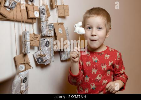 Ein Junge mit dem Hasen aus dem 2023-Symbol steht neben dem handgefertigten Weihnachtskalender Stockfoto