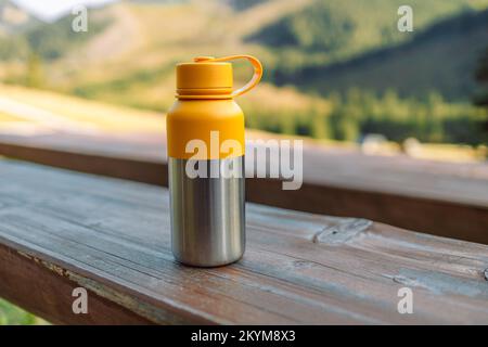 Wasserflasche auf Holzstumpf mitten im Wald. Wiederverwendbare Thermowasserflasche aus Stahl auf einem Holztisch im Wald. Thermowasserflasche aus Stahl. Be Stockfoto