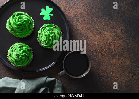 Drei Schokoladen-Cupcakes mit grüner Schlagsahne und Schokoladenstreuseln auf braunem Hintergrund. St. Patrick's Day. Speicherplatz kopieren. Blick von oben. Stockfoto