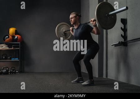 Der Mann, der die Barglocke hebt, als Teil des Cross-FIT-Trainings im dunklen Fitnessraum. Platz für Text Stockfoto