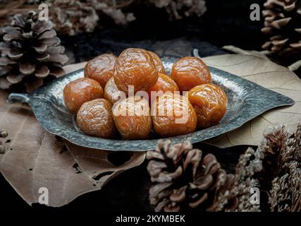 Drei aromatisierte, konservierte chinesische Pflaumen (konservierte Früchte) auf einem kleinen silbernen Blattteller. Sein Geschmack hat einen sauren, salzigen und süßen Geschmack. Selektives Fo Stockfoto