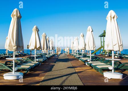 Hölzerne Panton mit Sonnenschirmen und Sonnenliegen in einem türkischen Hotel. Stockfoto