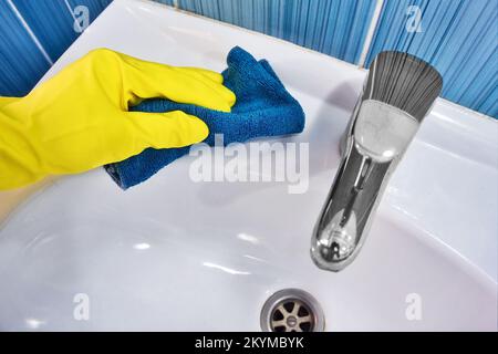 Handschuh aus gelbem Gummi mit Lappen, Wischtücher, weißes Waschbecken. Reinigung und Desinfektion mit Reinigungsmittel. Sauberes und glänzendes Waschbecken in der Toilette. Stockfoto