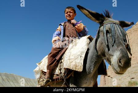 Bamyan (Bamiyan) / Zentralafghanistan: Ein kleiner Junge reitet auf einem Esel in der Nähe der Klippen in Bamyan Stockfoto