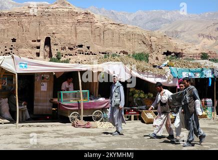 Bamyan (Bamiyan) / Zentralafghanistan: Eine Gruppe von Männern geht entlang einer Straße in Bamyan mit der kleinen Buddha-Nische dahinter Stockfoto