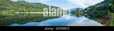 Panoramablick auf Berge, Bäume und Wolken, perfekt reflektiert in einem blauen See Stockfoto