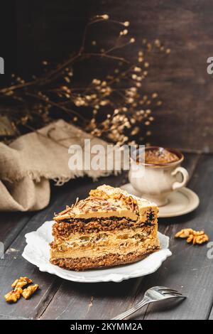 Eine Portion Walnusskuchen auf dem Teller mit einer Tasse Kaffee auf rustikalem braunem Hintergrund Stockfoto
