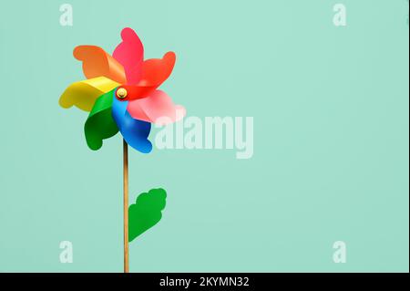 Mehrfarbiges, blumenförmiges Drehrad mit grünem Blatt auf hellem türkisfarbenem Hintergrund Stockfoto