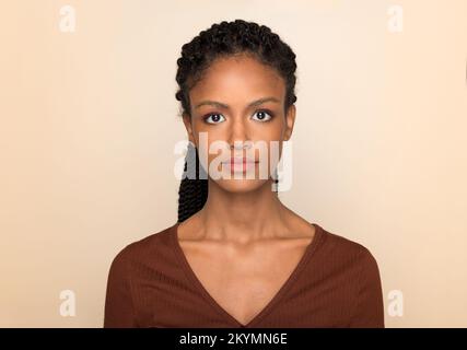 Porträt einer jungen afroamerikanischen Frau mit langen Afrogeflechten, die vor beigefarbenem Hintergrund in die Kamera schaut Stockfoto
