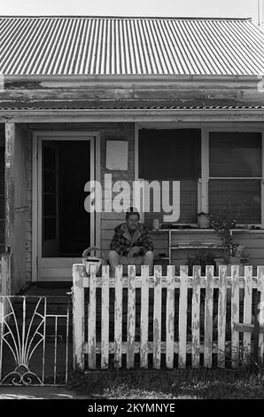 Ein alter Mann sitzt vor seiner heruntergekommenen Hütte: 64 Berner Street, Merewether, Newcastle, New South Wales, Australien. Schwarz-Weiß-Version Stockfoto