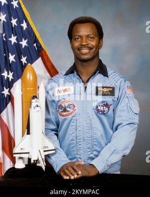 Ronald McNair Offizielles Porträtfoto des Astronauten Ronald E. McNair. Astronaut McNair ist im blauen Shuttle-Fluganzug, steht vor einem Tisch, der ein Modell des Space Shuttles enthält. Hinter ihm ist eine amerikanische Flagge zu sehen. Datum: 2. Juli 1985 Stockfoto