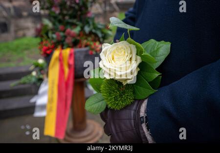 Trier, Deutschland. 01.. Dezember 2022. Ein Mann hält eine weiße Rose vor der Porta-Nigra, um den Opfern und Verletzten des Amoklaufs am 1. Dezember 2020 in der Innenstadt von Trier zu gedenken. Zwei Jahre nach dem Amoklauf in Trier erinnert sich die Stadt an die Opfer. Kredit: Harald Tittel/dpa/Alamy Live News Stockfoto