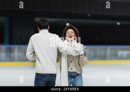 Eine afroamerikanische Frau, die lacht, während sie mit ihrem Freund Schlittschuhlaufen geht Stockfoto