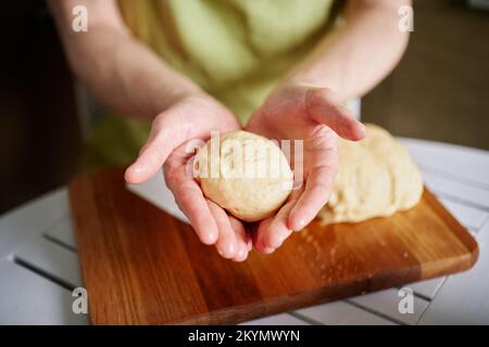 Nahaufnahmen von männlichem Küchenchef in grüner Schürze mit Teigball. Arbeiten zu Hause Küchenkonzept, hausgemachtes Backen. Nicht wiedererkennbare Person. Hochwertige Bilder Stockfoto