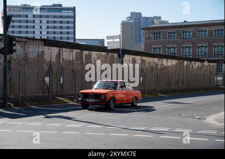 12.03.2022, Berlin, Deutschland, Europa - BMW 2002 Oldtimer fährt entlang der Niederkirchnerstraße im Bezirk Mitte, vorbei an einem Abschnitt der ehemaligen Mauer. Stockfoto