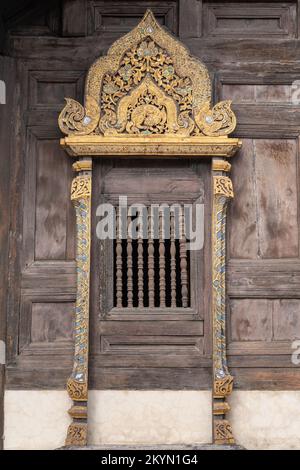 Wunderschönes Fenster mit vergoldeten geschnitzten Holzpaneelen an der buddhistischen Tempelfassade Wat Phan Tao, Chiang Mai, Thailand Stockfoto