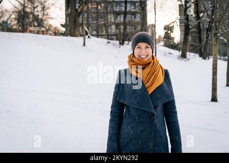 Eine junge Frau in Winterkleidung lächelt weit und schaut in die Kamera Stockfoto