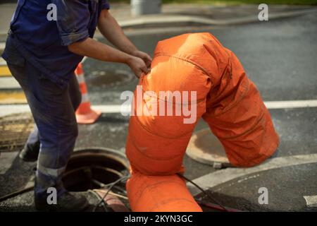 Kanalisationsreparatur. Abwasser aus der Luke Pumpen. Luke öffnen. Arbeiter steuert die Luftzufuhr. Stockfoto