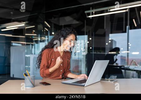 Hispanische Geschäftsfrau feierte Sieg und Erfolg, Büroangestellte erhielten Online-Nachrichten und ein glückliches Lächeln und schauten auf den Laptop-Bildschirm, der die Hand als Triumph-Geste hielt. Stockfoto