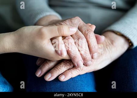 Junge Hand, die alte Hände einer Frau hält. Weichzeichner. Das Konzept der Unterstützung im Alter Stockfoto