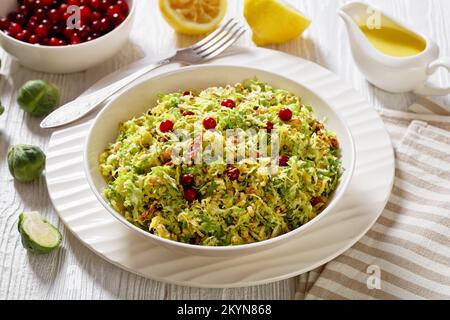 rosenkohl-Krautsalat mit Mandeln, knuspriger gebratener Speck und Cranberries in einer weißen Schüssel auf einem Holztisch mit Olivenöl-Zitronendressing, Landschaftsblick fr Stockfoto