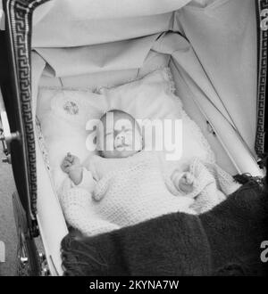 1950er, historisch, Blick von oben auf ein Baby, das auf dem Rücken eines weichen Kissens in einem Kinderwagen liegt, mit einer lackierten Baumwolldecke darüber und dem Klappdach des Kinderwagens oben, England, Großbritannien. Stockfoto