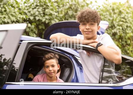 Porträt eines Teenagers, der sich an die Tür lehnt, während der Bruder im Auto sitzt Stockfoto