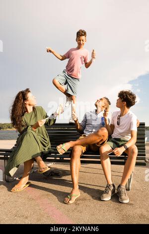 Die Familie sieht sich den Jungen an, der während des Urlaubs auf der Bank balanciert Stockfoto