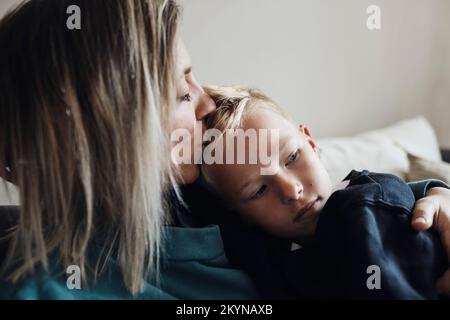 Mutter küsst Sohn, der zu Hause auf dem Sofa sitzt Stockfoto