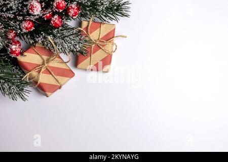 Zwei handwerklich gepackte weihnachtsgeschenke in gestreiftem Rot- und Kraftpapier mit einem Zweig grüner Fichtenpelzbäume mit Schnee und Strauchweide auf Weiß Stockfoto